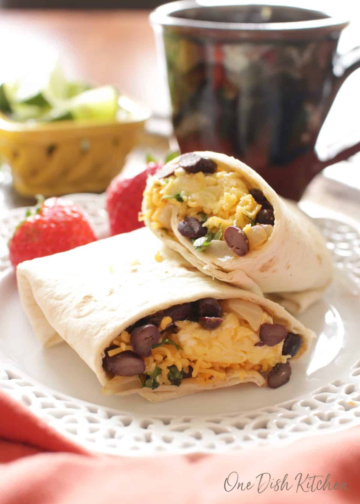 a burrito with scrambled eggs, cheese, and beans on a plate next to a cup of coffee.
