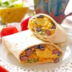 egg, sausage and cheese wrapped up in tortillas on a white dish.