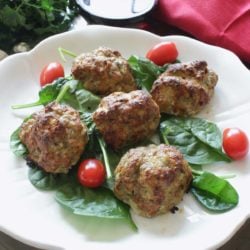 a white plate filled with meatballs over fresh spinach and cherry tomatoes