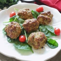 a small batch of ground turkey meatballs on a white plate with fresh spinach and tomatoes.