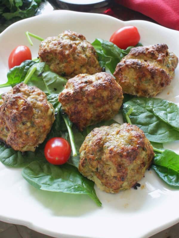 a small batch of ground turkey meatballs on a white plate with fresh spinach and tomatoes.