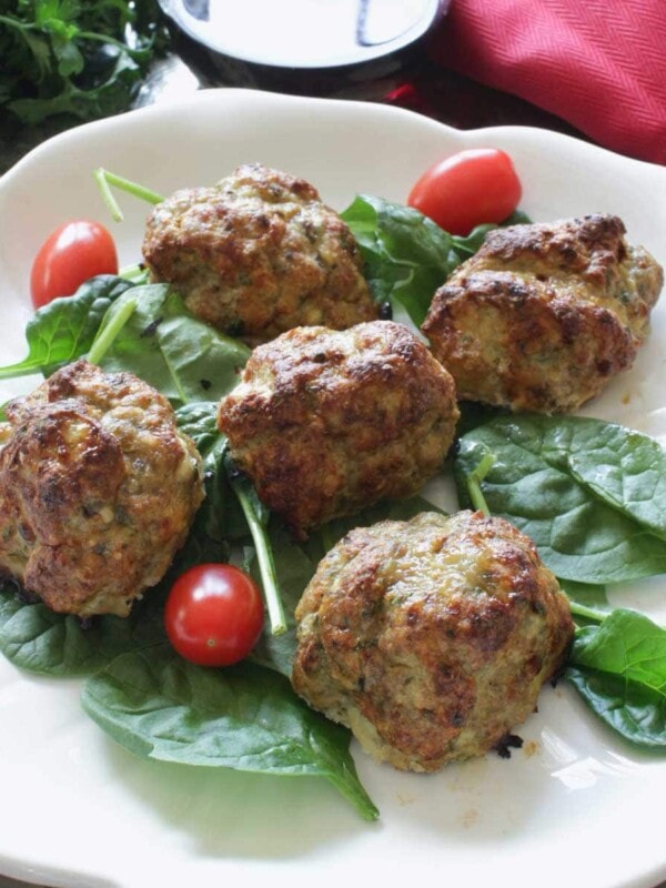 a white plate filled with meatballs over fresh spinach and cherry tomatoes