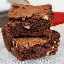 two brownies with nuts stacked on top of each other on a plate