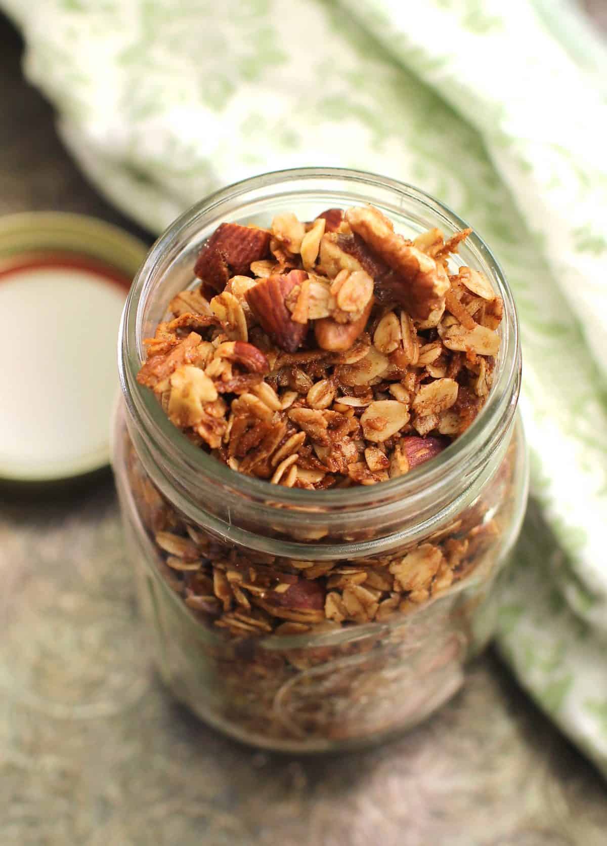 an overhead view of granola in a small mason jar next to a green and white napkin.
