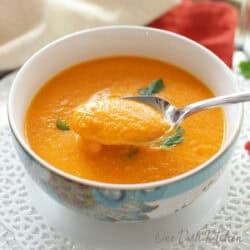 A bowl of carrot soup garnished with cilantro on a glass tray next to a glass of white wine and a bunch of cilantro.