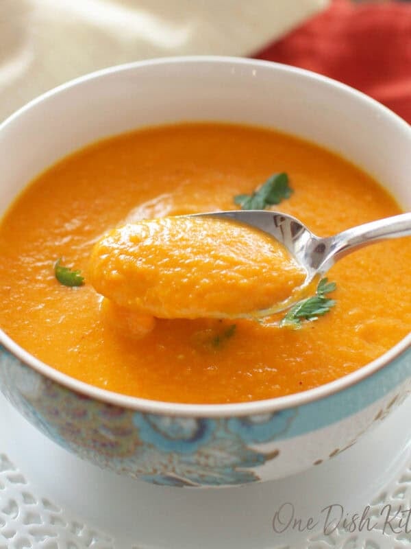 A bowl of carrot soup garnished with cilantro on a glass tray next to a glass of white wine and a bunch of cilantro.