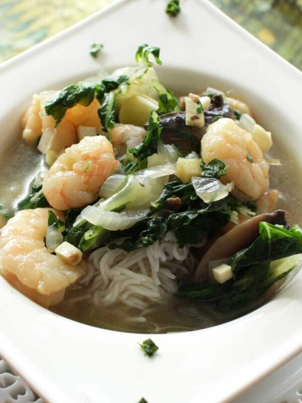 a white bowl filled with thai soup with shrimp over rice noodles