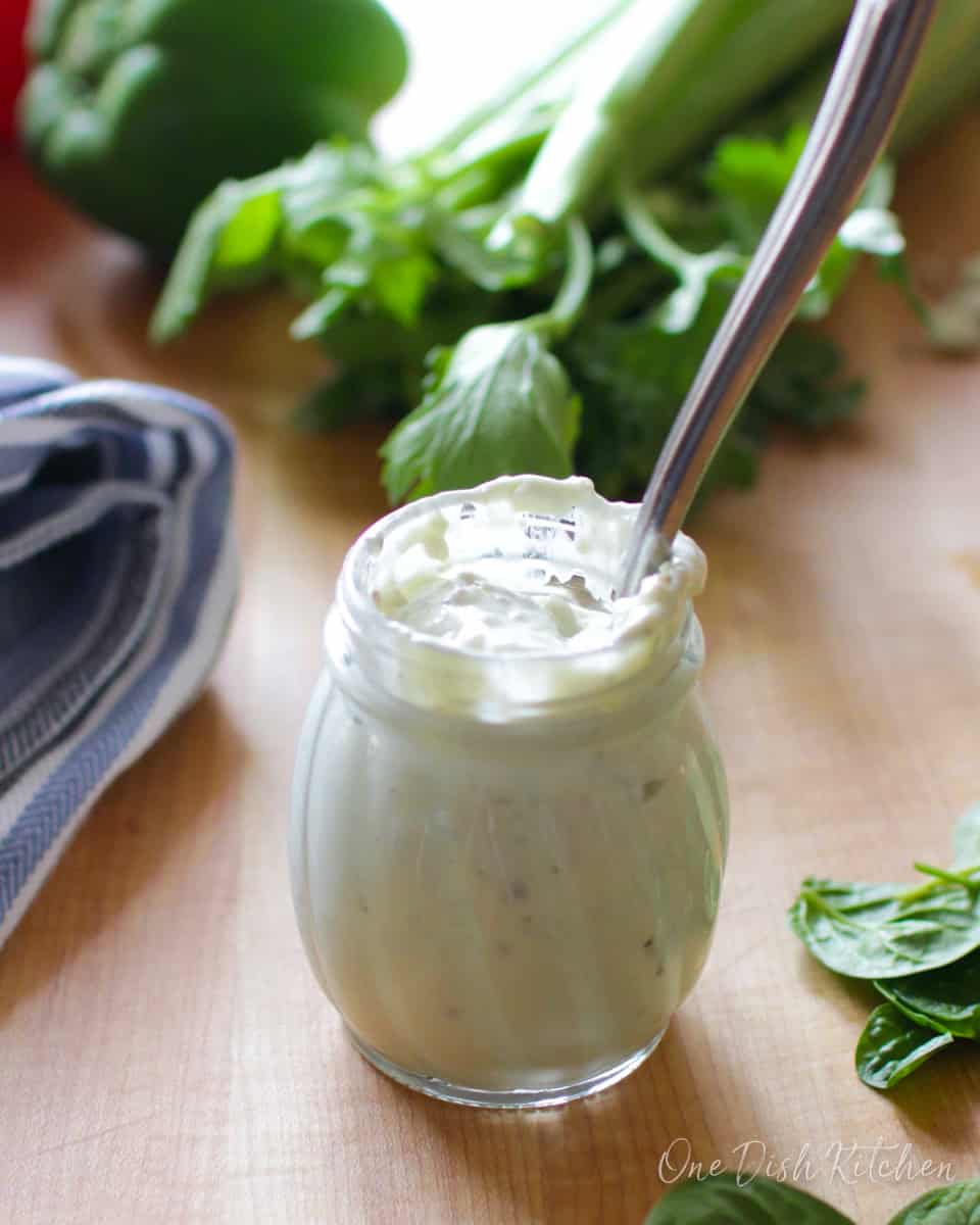 a jar of blue cheese dressing on a brown cutting board surrounded by fresh vegetables.