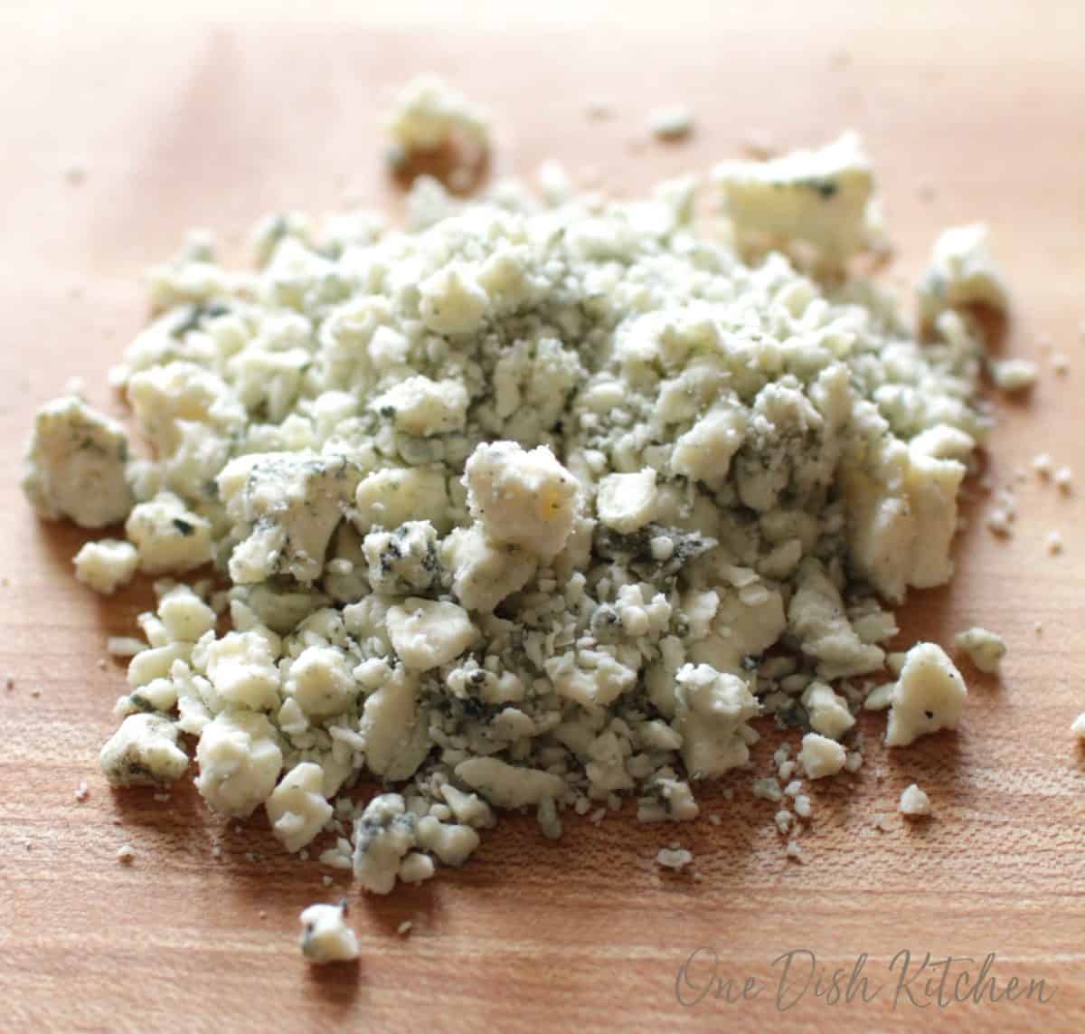 blue cheese crumbles on a brown wooden cutting board.