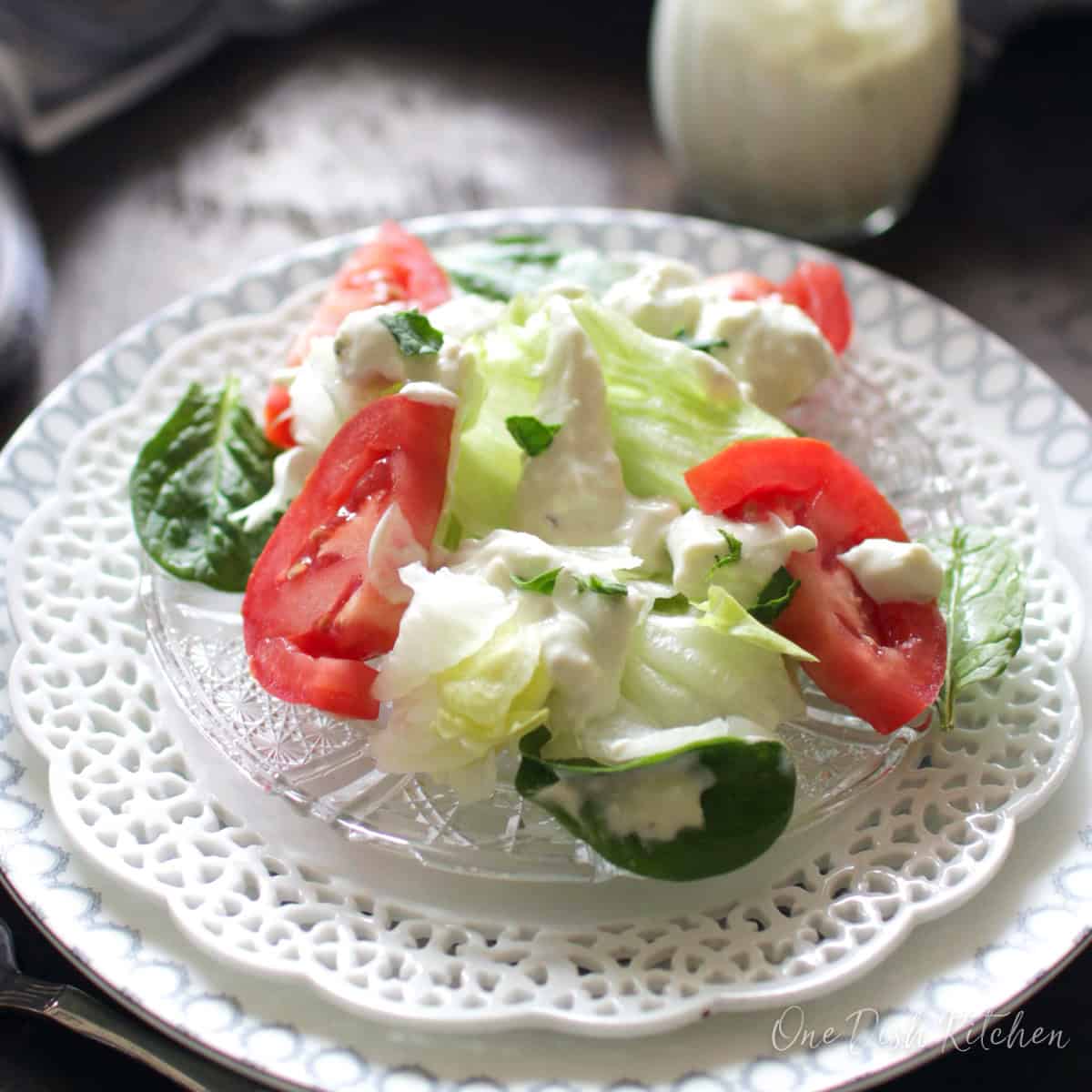 lettuce and tomatoes on a clear plate next to a jar of salad dressing.