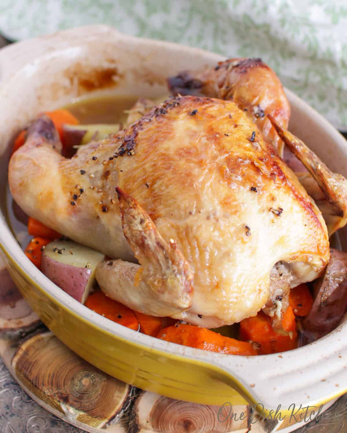 a roasted cornish hen on top of vegetables in a roasting pan.