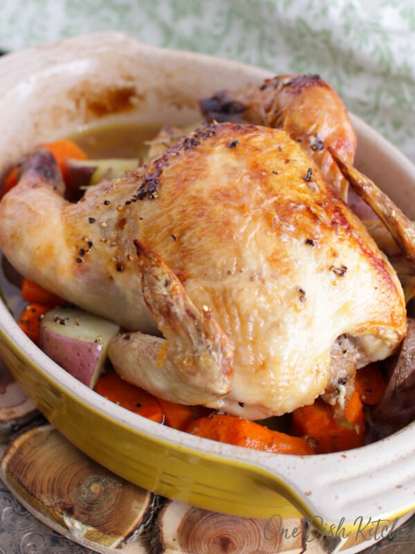 a roasted cornish hen on a bed of carrots in a small baking dish