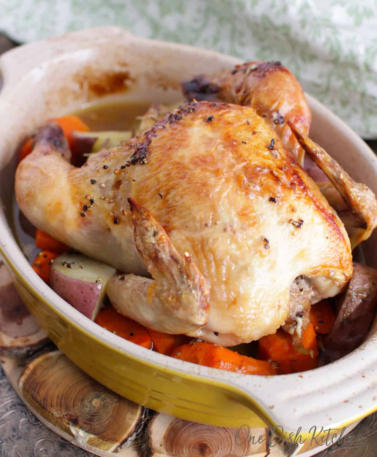 a roasted cornish hen on a bed of carrots in a small baking dish.