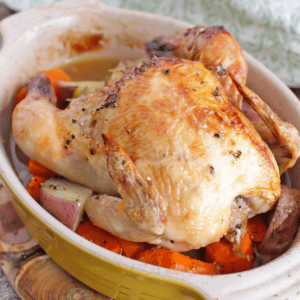 a roasted cornish hen on a bed of carrots in a small baking dish.