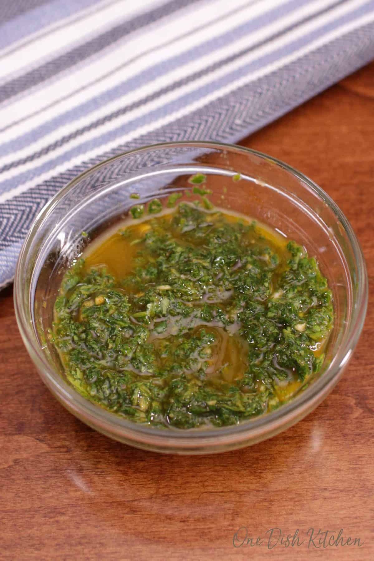 a bowl of chermoula on a brown table next to a blue and white kitchen towel.