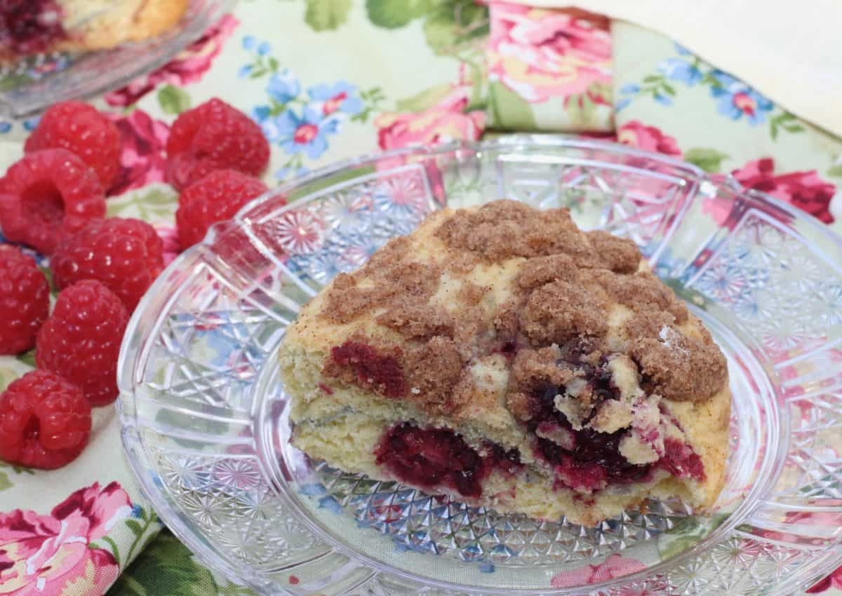 one scone filled with berries on a clear plate next to a handful of raspberries.