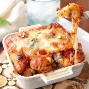 Mini pizza monkey bread in a small baking dish with a cheesy pull-apart piece being lifted, made with biscuit dough, pepperoni, and mozzarella cheese.