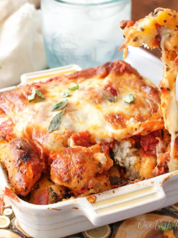 Mini pizza monkey bread in a small baking dish with a cheesy pull-apart piece being lifted, made with biscuit dough, pepperoni, and mozzarella cheese.