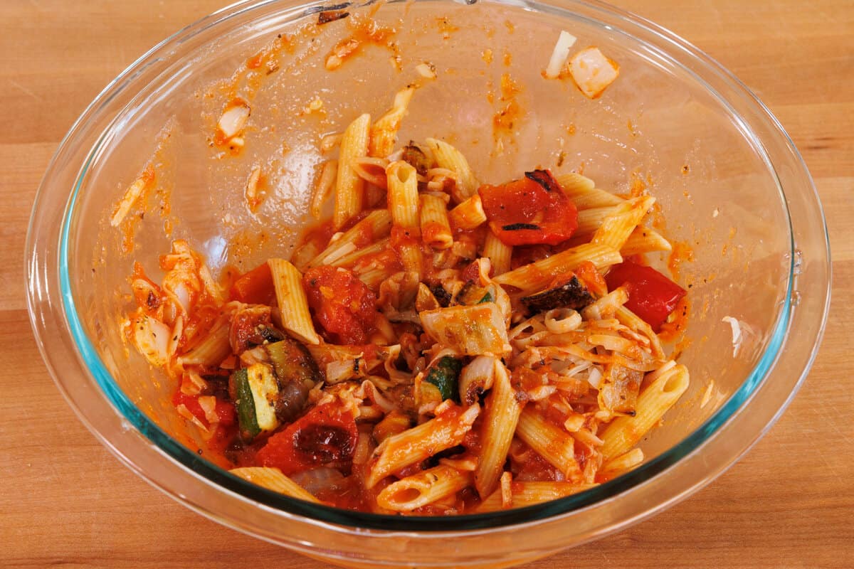 penne with roasted vegetables, cheese, and sauce in a mixing bowl