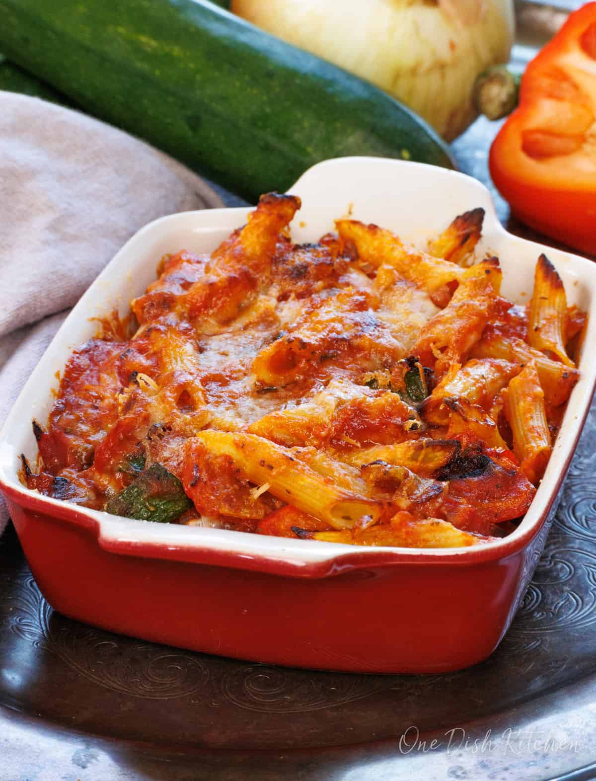 a pasta and cheese casserole in a red baking dish next to a brown napkin.