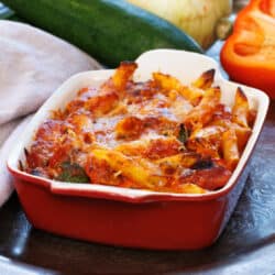 baked pasta with vegetables in a red baking dish next to a brown napkin