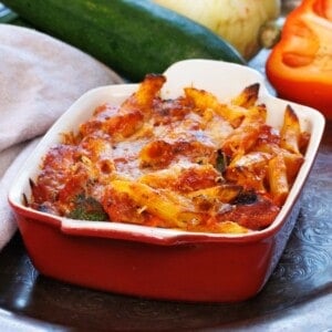 baked pasta with vegetables in a red baking dish next to a brown napkin.