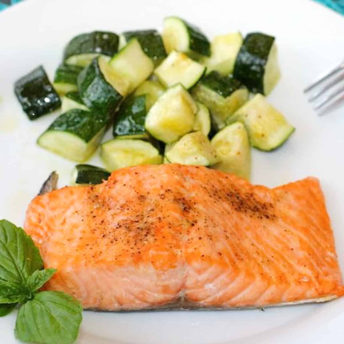 broiled salmon seasoned with salt, pepper and lemon juice on a plate with diced zucchini.
