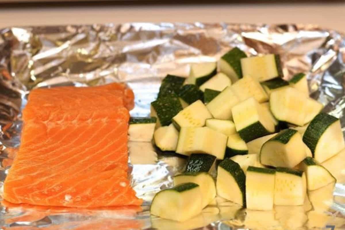 Prepping salmon for one: A 4oz salmon fillet skin-side down on a toaster oven tray next to half-inch diced zucchini pieces.