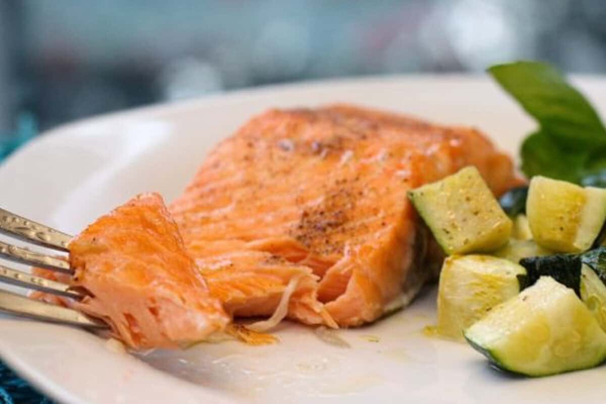 a single serving of broiled salmon on a plate with a fork showing the texture and flakiness of the fish.
