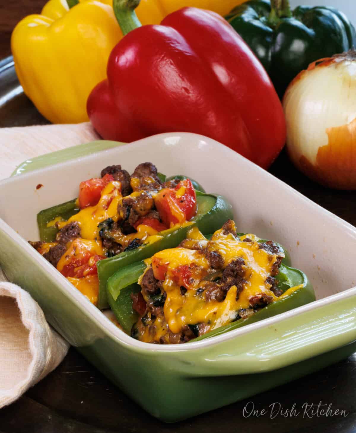 stuffed bell peppers in a baking dish next to a red, yellow, and green pepper on a silver tray