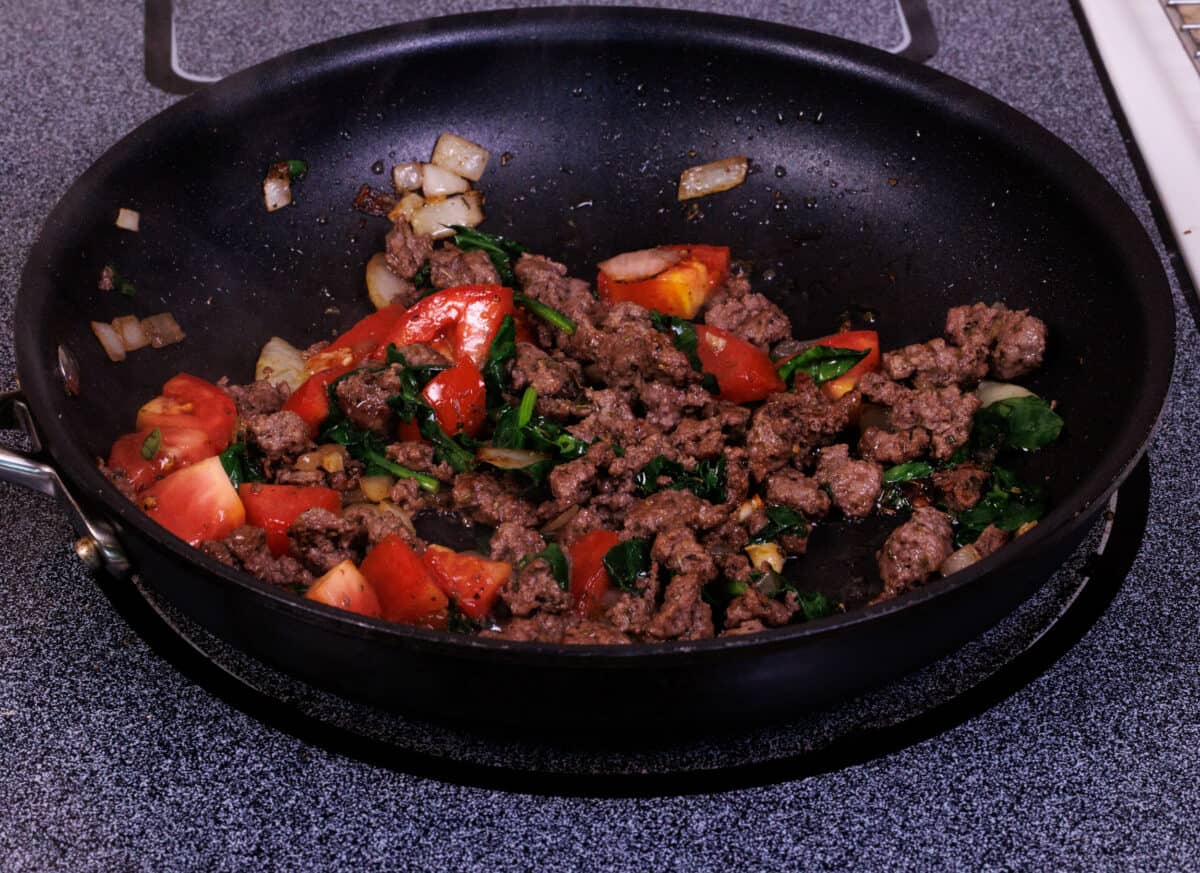 ground beef, spinach, and tomatoes sauteeing in a pan