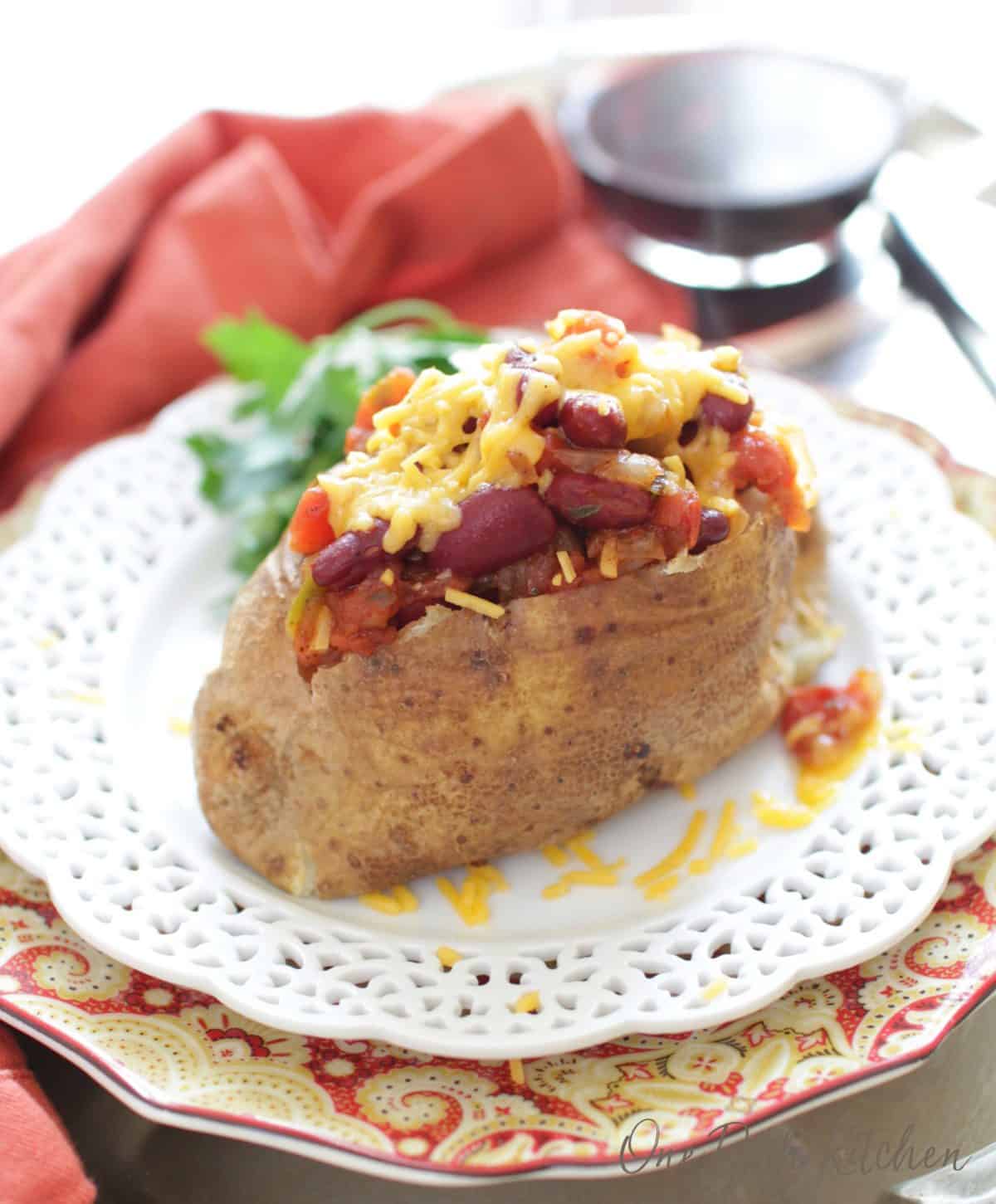 a baked potato topped with beans and cheese on a white plate next to a glass of wine.