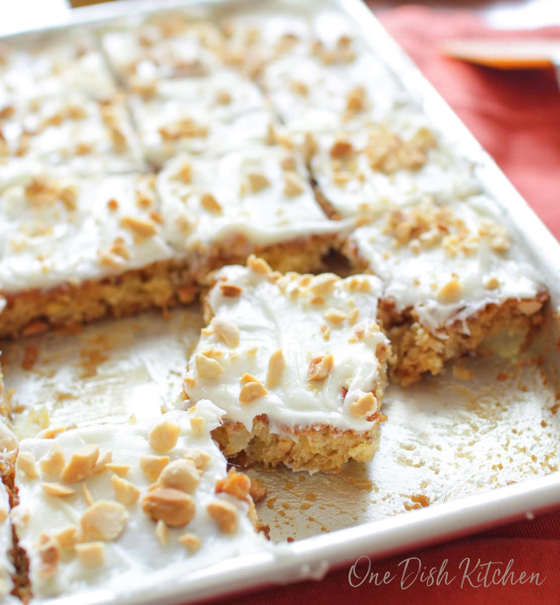 a small pineapple cake on a sheet pan topped with nuts and sliced into squares.