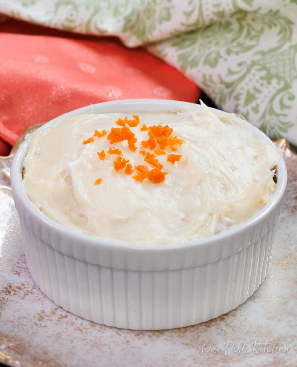 a small carrot cake in a round ramekin topped with grated carrots.