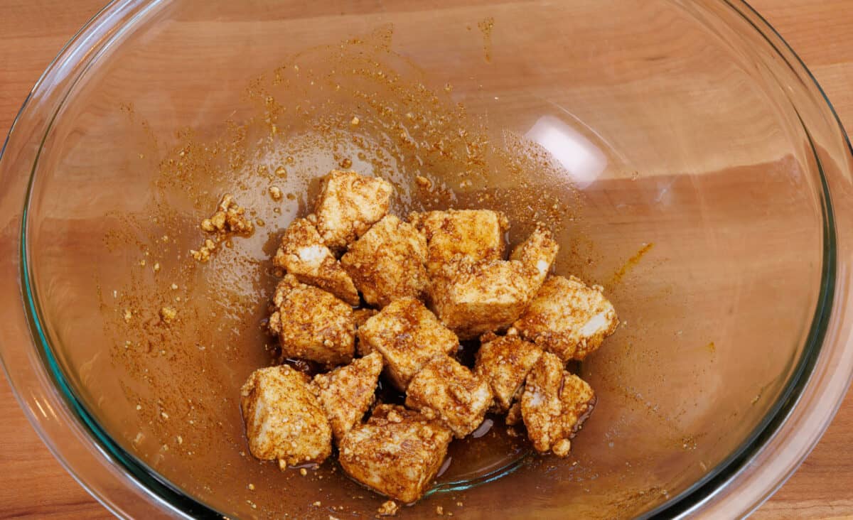 cubes of paneer marinating in spices and olive oil in a clear bowl