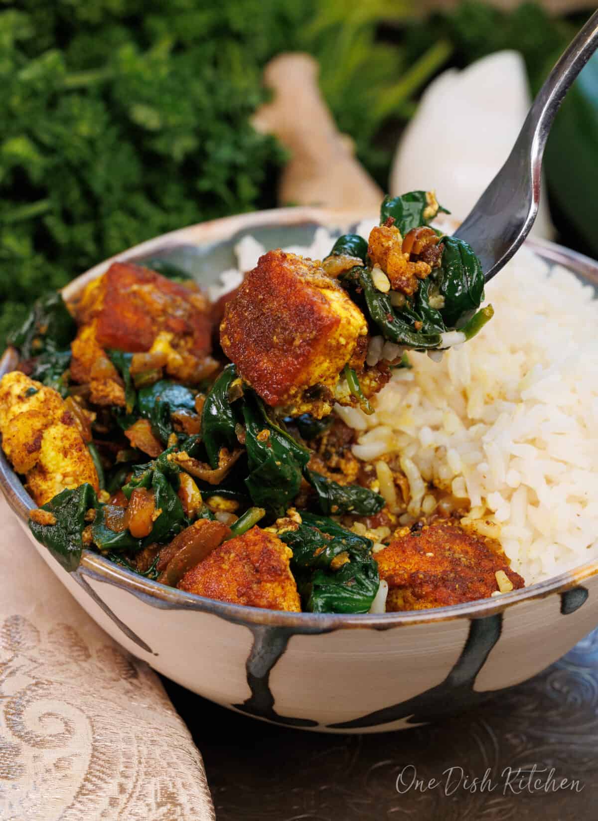 a fork filled with paneer and spinach over the bowl of saag paneer