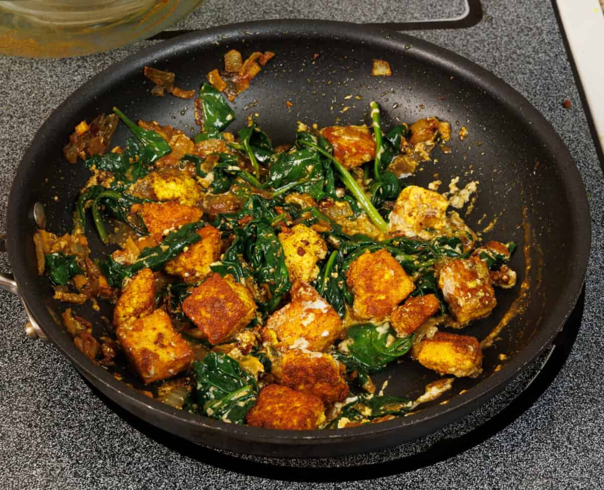 cubes of paneer cooking along with spinach in a skillet