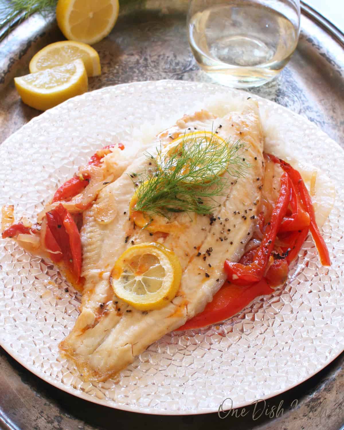 baked catfish topped with lemon slices on a bed of vegetables.