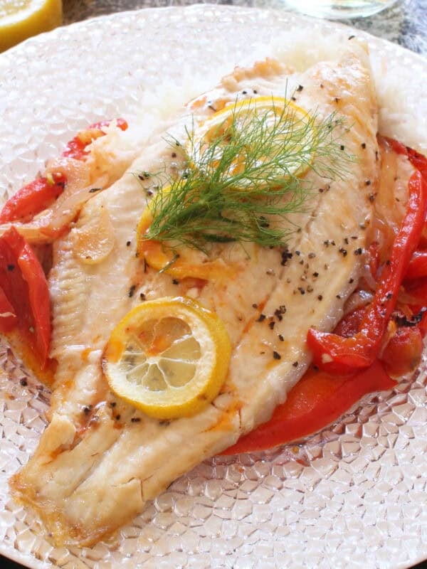 baked catfish topped with lemon slices on a bed of vegetables.