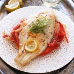 baked catfish on a white plate surrounded by vegetables.