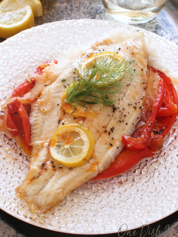 baked catfish on a white plate surrounded by vegetables.