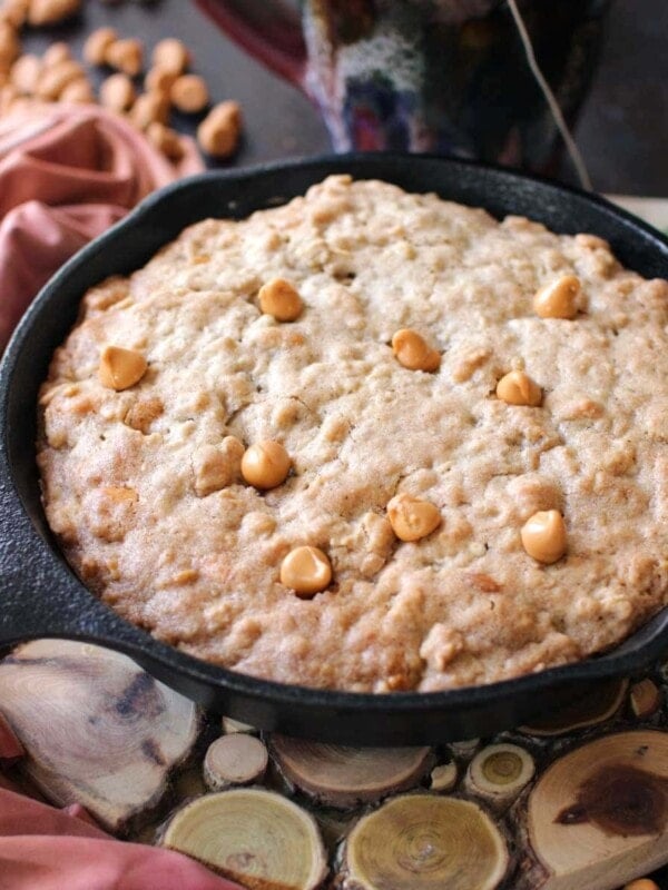 a butterscotch and oatmeal cookie baked in a skillet on top of a wooden trivet.