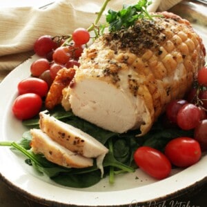 A turkey roast on a plate surrounded by cherry tomatoes and spinach.