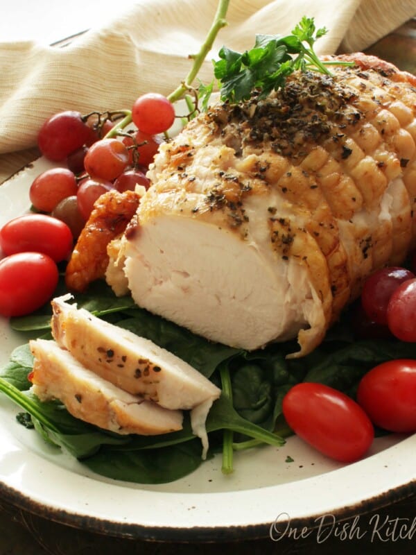 A turkey roast on a plate surrounded by cherry tomatoes and spinach.