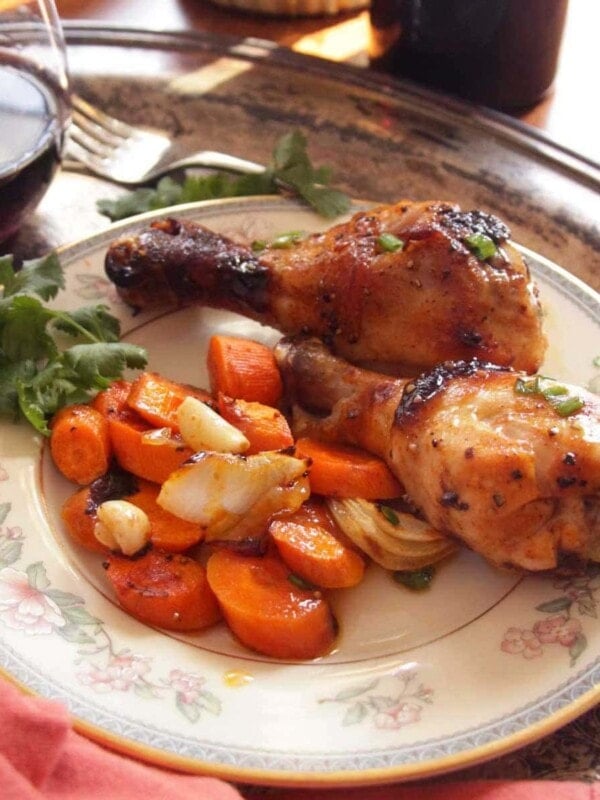 Two bbq chicken drumsticks on a plate next to roasted carrots and garlic