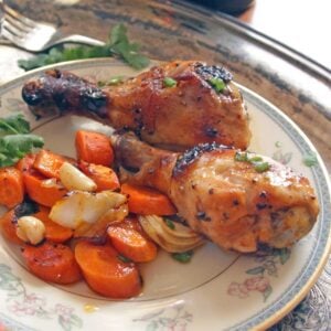 two baked chicken legs with roasted vegetables on a plate.
