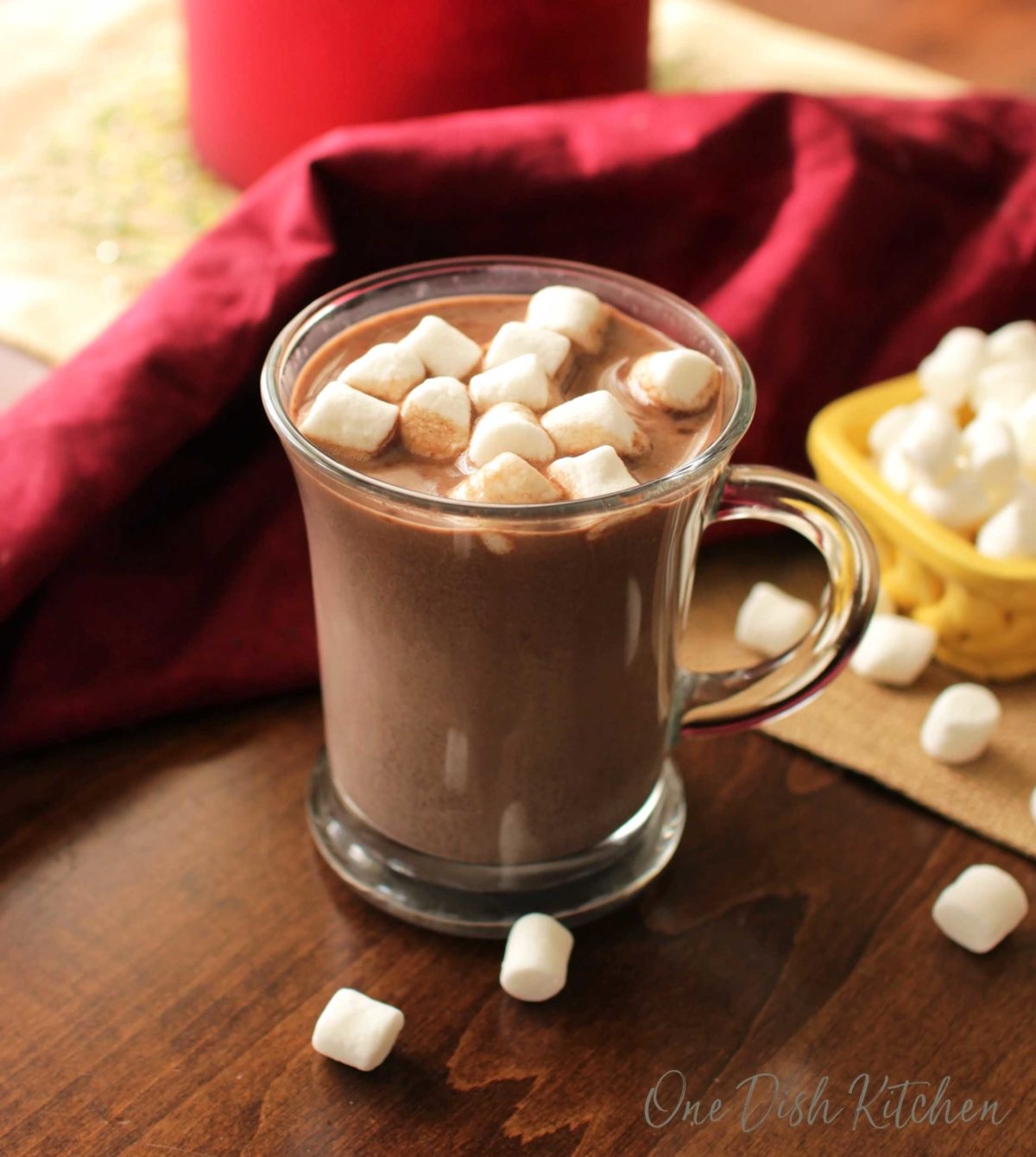 a mug of hot chocolate next to marshmallows in a container that have spilled onto the table.