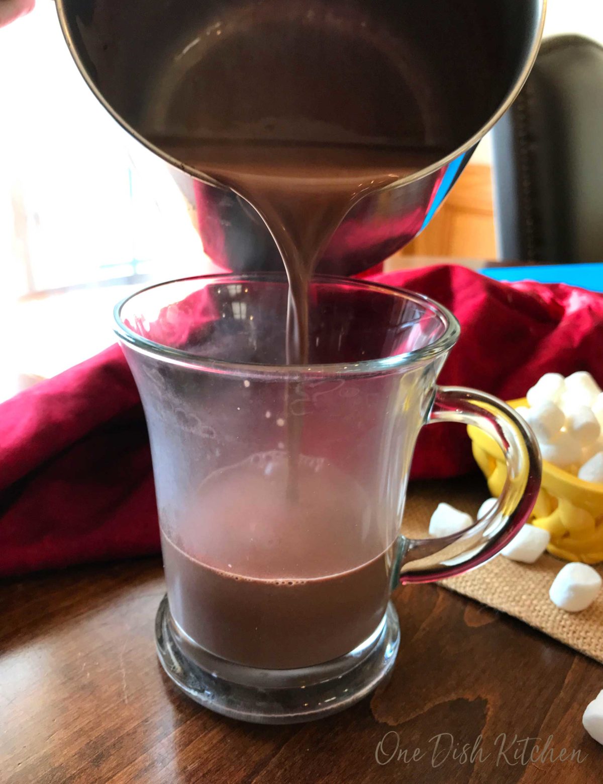 pouring hot chocolate from a saucepan into a mug on a kitchen table.