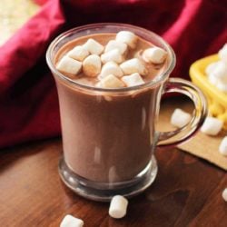 a mug of hot chocolate next to marshmallows in a container that have spilled onto the table