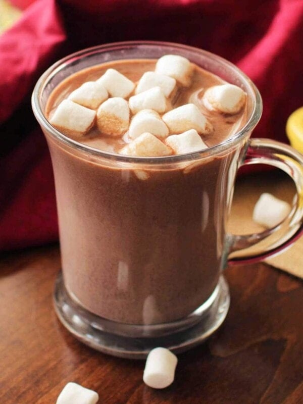 a mug of hot chocolate next to marshmallows in a container that have spilled onto the table
